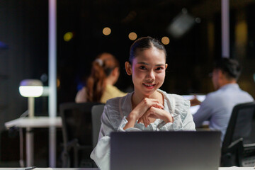 Asian businesswoman working late in a modern office looking at camera and smiling. Dedication and hard work concept