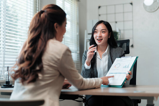 Two business women having a productive discussion, analyzing charts and data on a clipboard in a modern office meeting