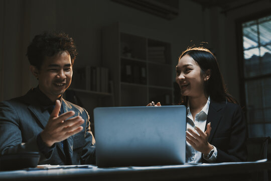 Two diverse business colleagues discussing work project details, brainstorming ideas in a darkened office at night