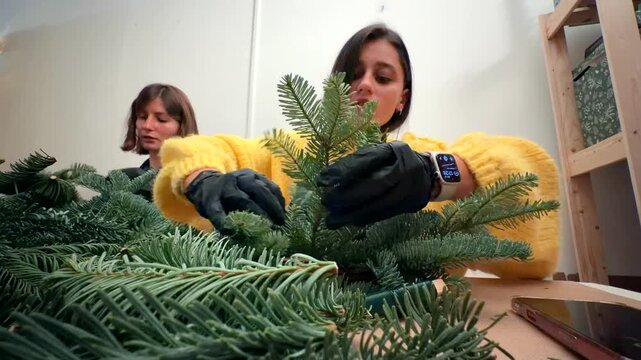 Hands assembling evergreen wreath in workshop with gloves