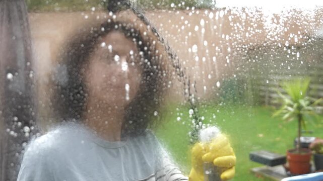 Woman cleans house windows with spray bottle and squeegee during the day