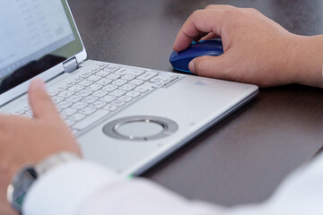 デスクでノートパソコンをマウス操作する男性の手元