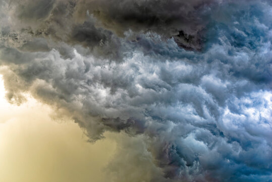 detail of intense dark storm clouds lit from behind with glowing yellow sun light from behind lighting the rain bands