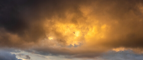 Epic panoramic view golden rain clouds during sunset or sunrise breaking through dark storm clouds creating powerful heavenly background with bright light