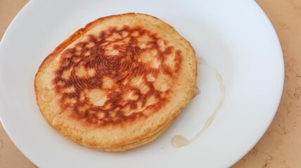 Close up of a piece of imperfect homemade pancake on a white plate  with honey on the side