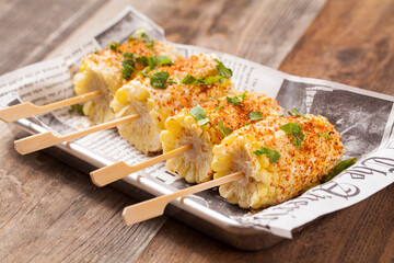 Four corn on the cob pieces on a newspaper plate on a wooden table. 