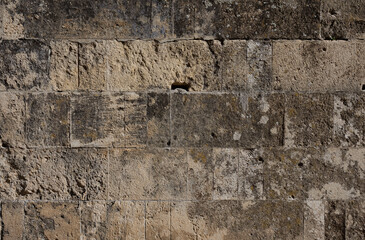 Rough texture of an old stone masonry wall with uneven color, stains, and weathered patterns. Natural surface shaped by time and elements, ideal for backgrounds, overlays, design and artistic uses.