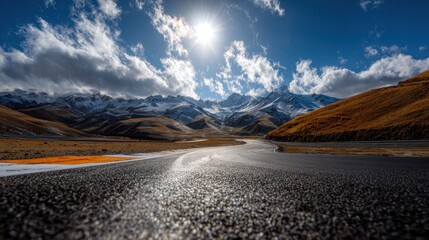 Asphalt road leading toward sunlit snowcapped mountain range