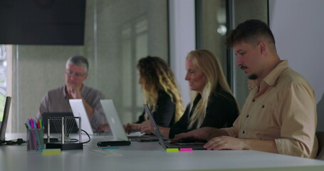 Office employees work in focused silence during modern team meeting with laptops open on table and natural light filling professional workspace