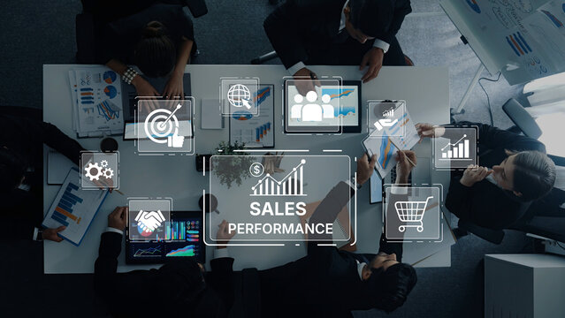 Aerial view of a business team collaborating on sales performance analysis with digital devices showcasing graphs, data, and strategic insights in a modern office environment. Trope