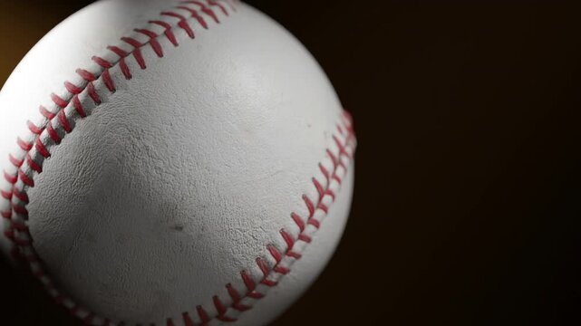 A close-up baseball rests under dramatic lighting, shadows carving deep texture across the leather and stitches. Atmospheric, cinematic, and perfect for intense sports visuals or intro sequences.