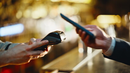Customer hand tapping terminal smartphone at night bar closeup. Cashless payment