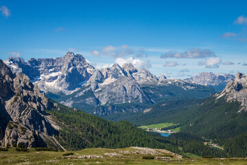 Panoramic view from Tre Cime di Lavaredo towards the Sorapiss at left; Lake Misurina and Cima Ambrizzola in the background right; Dolomite peaks above meadows against blue sky in Italy