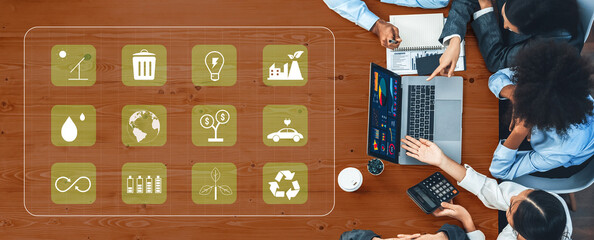 A diverse team of professionals gathers around a laptop, discussing sustainability strategies and analyzing data charts in a modern office setting focused on eco-friendly solutions. Trope