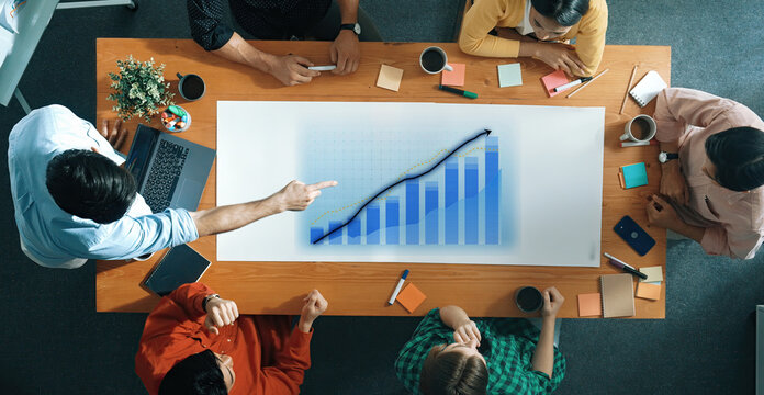 Team of professionals discussing strategies and analyzing growth data during a business meeting in a modern workspace with laptops and coffee cups. Axiom