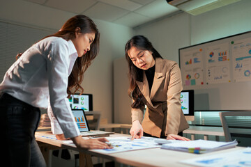 Businesswomen discussing data analysis during late office meeting