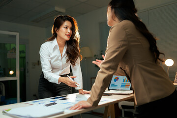 Businesswomen discussing data analysis during late night meeting