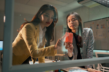 Businesswomen collaborating on strategy writing on glass board