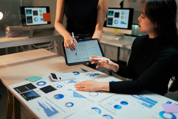 Women analyzing marketing data using tablet and charts