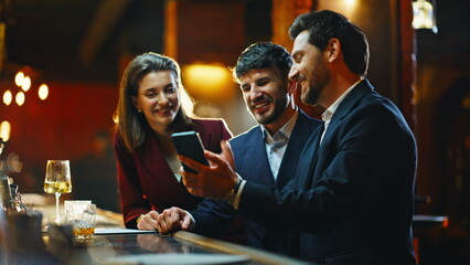Happy coworkers spending evening at pub closeup. Employees looking smartphone