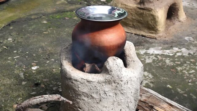 Food preparation that is rice, pongal or khichdi at traditional clay Chulha by burning wood log. vintage rustic look of rural India outdoor kitchen activity.