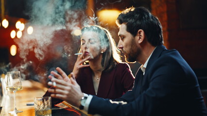 Well-dressed pair enjoying cigarette smoke relaxing at cafe bar counter closeup