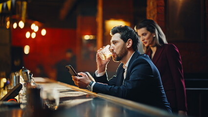 Elegant man sitting bar counter drinking cognac with smartphone alone closeup