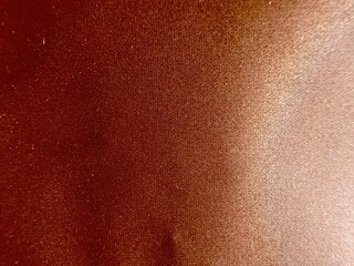 close-up of bronzed human skin with smooth gradient from dark brown to light tan and subtle central dimple on textured surface