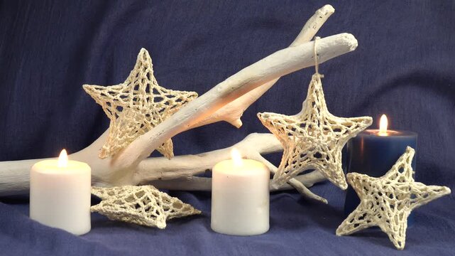 Handmade Christmas decorations white knitted star sway on a decorative white tree branch, burning candles against a blue backdrop 