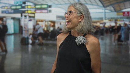 Woman with bare shoulders laughing and looking sideways in airport terminal while wearing glasses; joy travel anticipation.