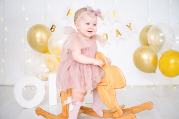 a little blue-eyed girl rides a wooden horse and celebrates her first birthday