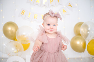 little blue-eyed girl celebrates her first birthday in bright room with ballon