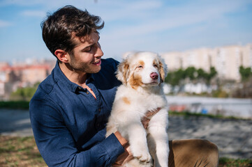 Young man holding australian shepherd puppy outdoors