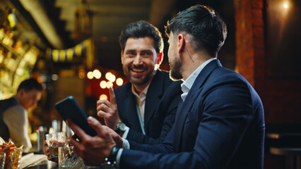 Business people chilling pub watching smartphone videos closeup. Laughing men