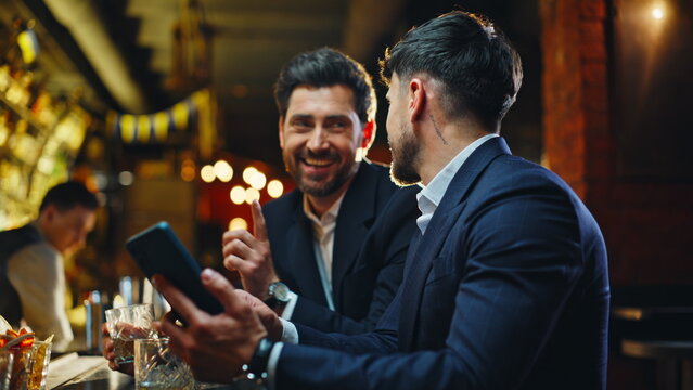 Business people chilling pub watching smartphone videos closeup. Laughing men