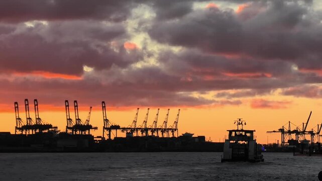 Dramatische Abendstimmung hinter der Silhouette der Hafenkr&auml;ne im Hafen von Hamburg, Hafenf&auml;hre f&auml;hrt vorbei