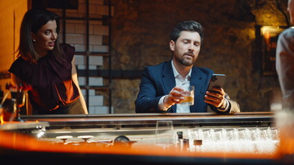 Man using mobile alone sipping brandy in bar closeup. Surprised couple meeting