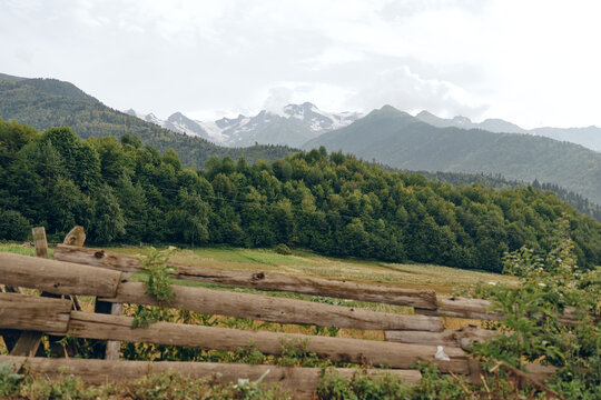 Landscape with a wooden fence in a tranquil countryside, forested hills and distant mountains under a calm sky, showcasing rustic scenery and nature
