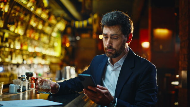 Tired businessman ordering alcohol in night bar closeup. Man reading smartphone