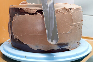 Confectioner woman is smearing cream on sides of cake using spatula, closeup view. culinary, baking and cooking food concept, home cooking