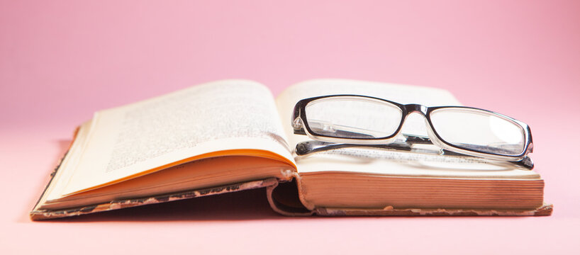 Open book with eyeglasses on pink background, education and reading concept