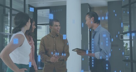 Discussing four staff in business wear in office lobby, holding tablet near column and glass walls