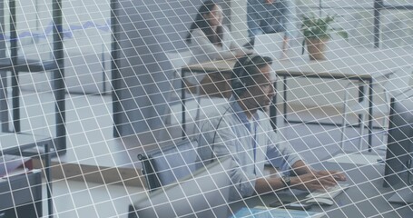 Typing worker wearing light shirt in office using keyboard and monitor through wire-grid glass