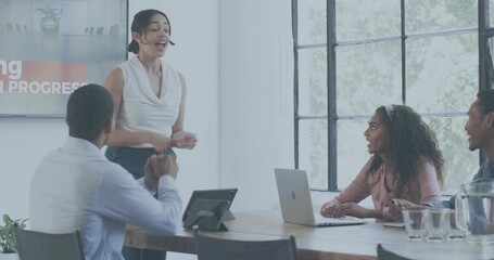 Presenting woman in sleeveless white blouse and dark pants speaking in conference room with laptop