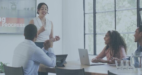 Presenting woman wearing white blouse and dark bottoms gesturing in conference room with monitor