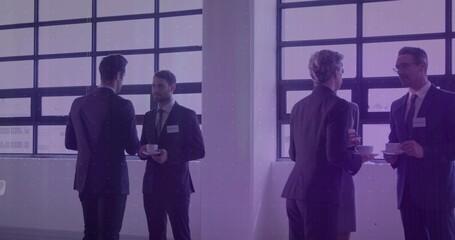 Holding white cups, group wearing suits networking near grid windows with name badges