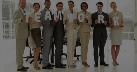 Holding office team wearing suits standing by glass walls near table, displaying letters TEAMWORK