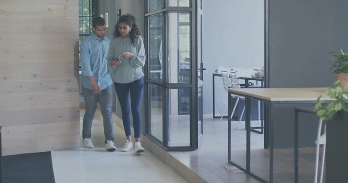 Walking two coworkers checking phone in office near glass wall, wearing blue shirt, copy space
