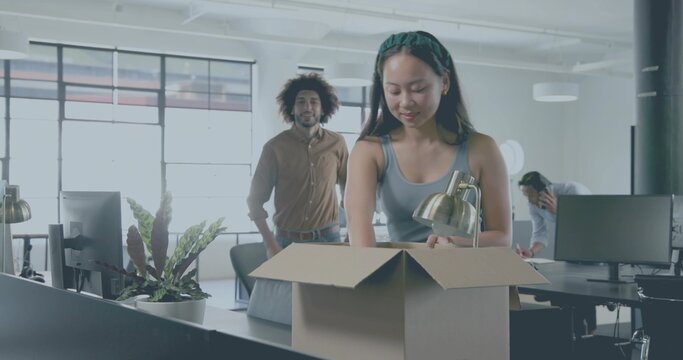 Packing woman gray tank top green headband placing brass lamp into cardboard box, office