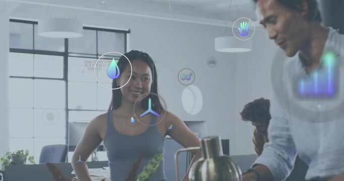 Standing woman in sleeveless grey top guiding team in open-plan office, with kettle and AR icons
